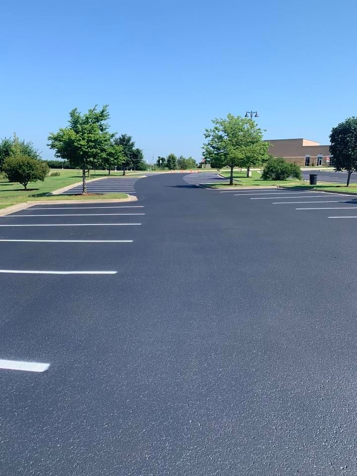 Empty parking lot with white lines, trees, and a building in the distance on a sunny day