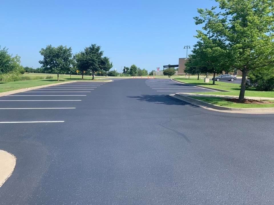 Empty parking lot with fresh black asphalt, white lines, and trees under a clear blue sky