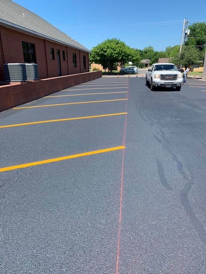 Parking lot beside a brick building with yellow lines and a white pickup truck on a sunny day