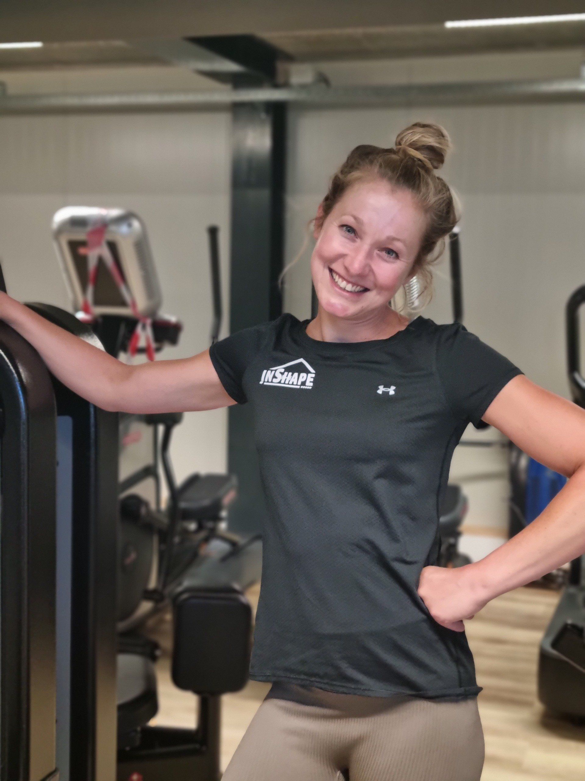 Een vrouw in een zwart onderpantsershirt lacht in een sportschool