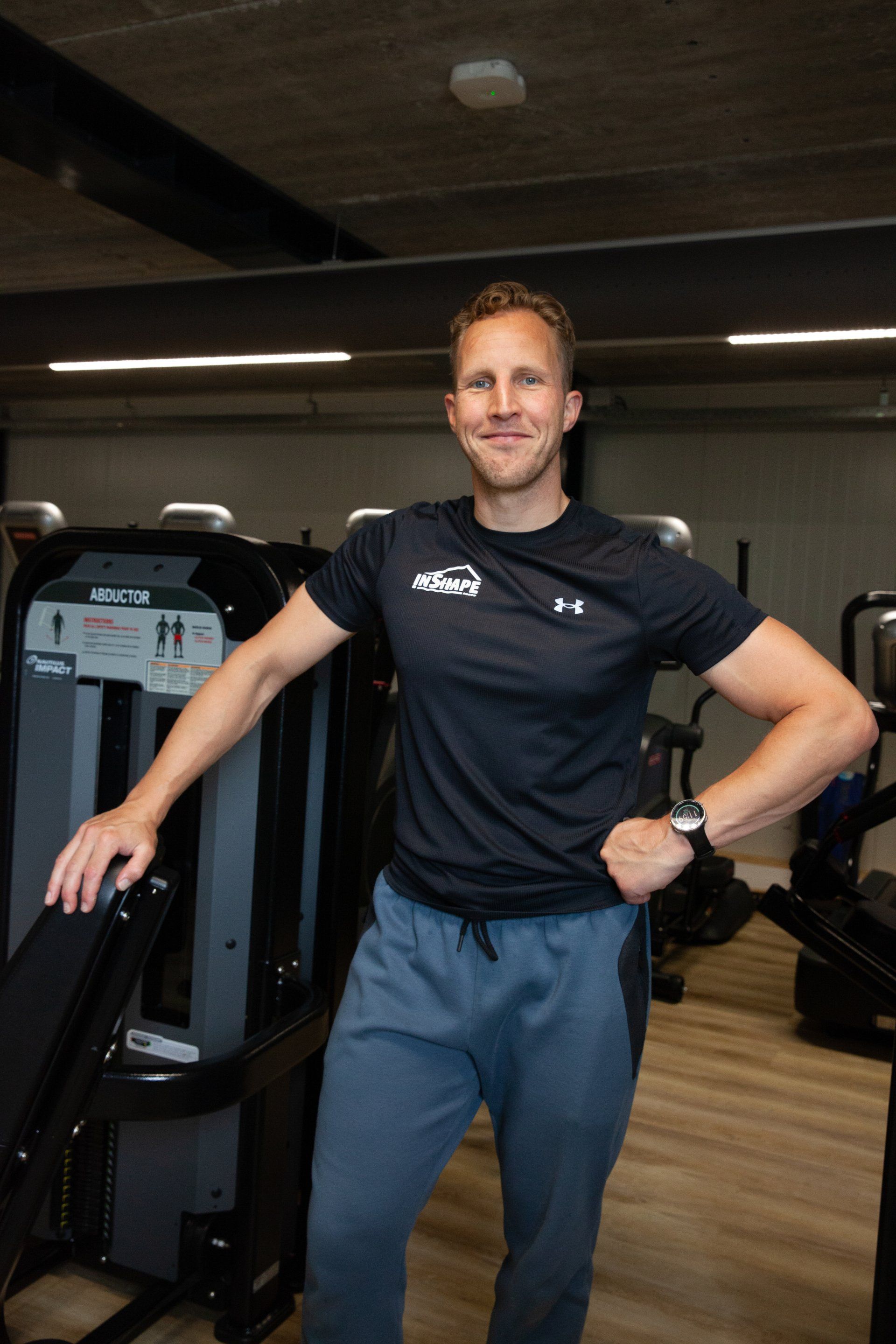 Een man staat in een sportschool met zijn handen op zijn heupen.