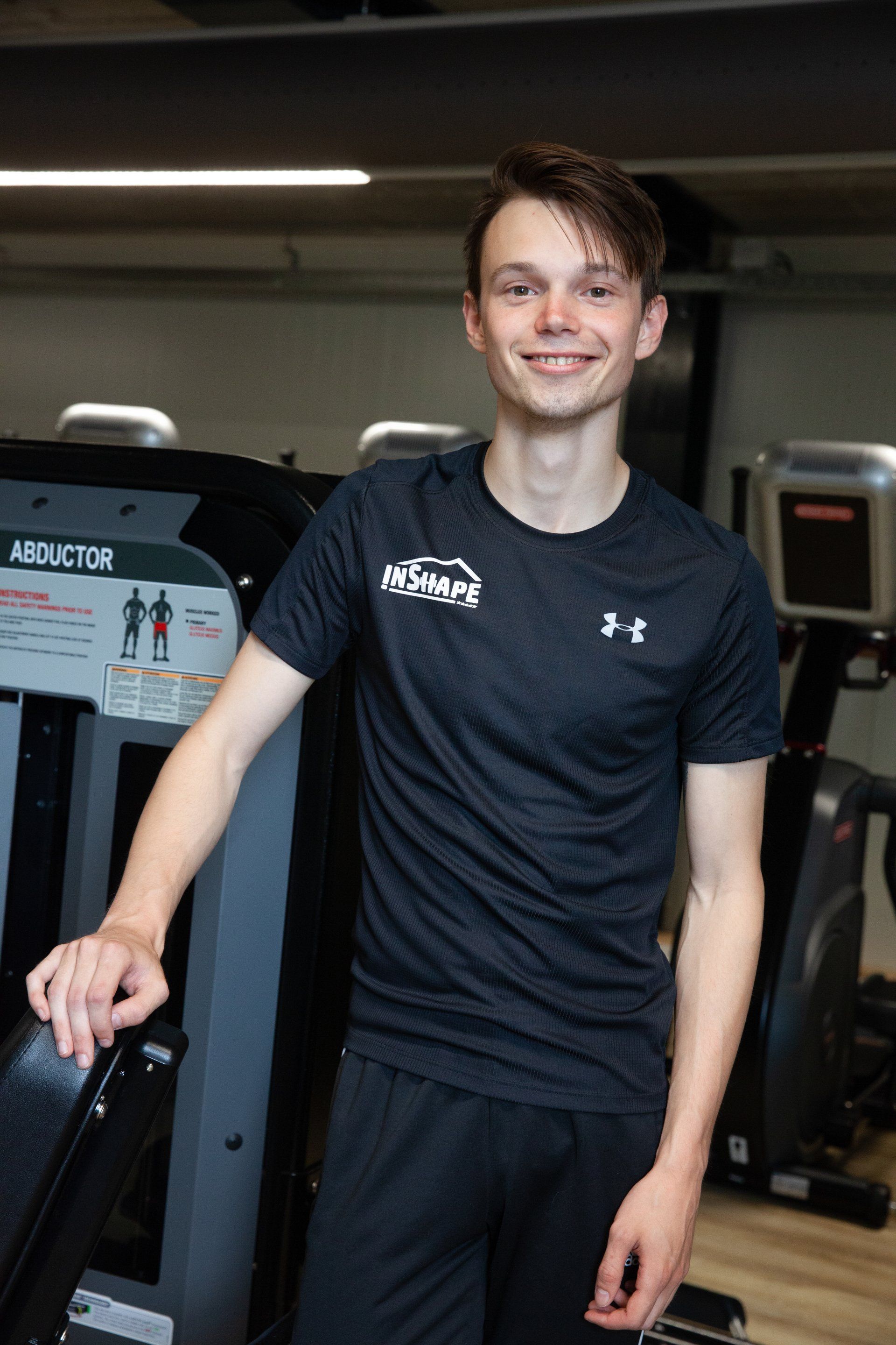 Een jonge man staat voor een loopband in een sportschool.