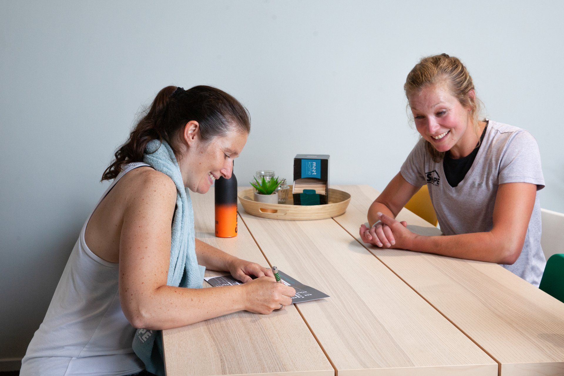 Twee vrouwen zitten aan een tafel en praten met elkaar.