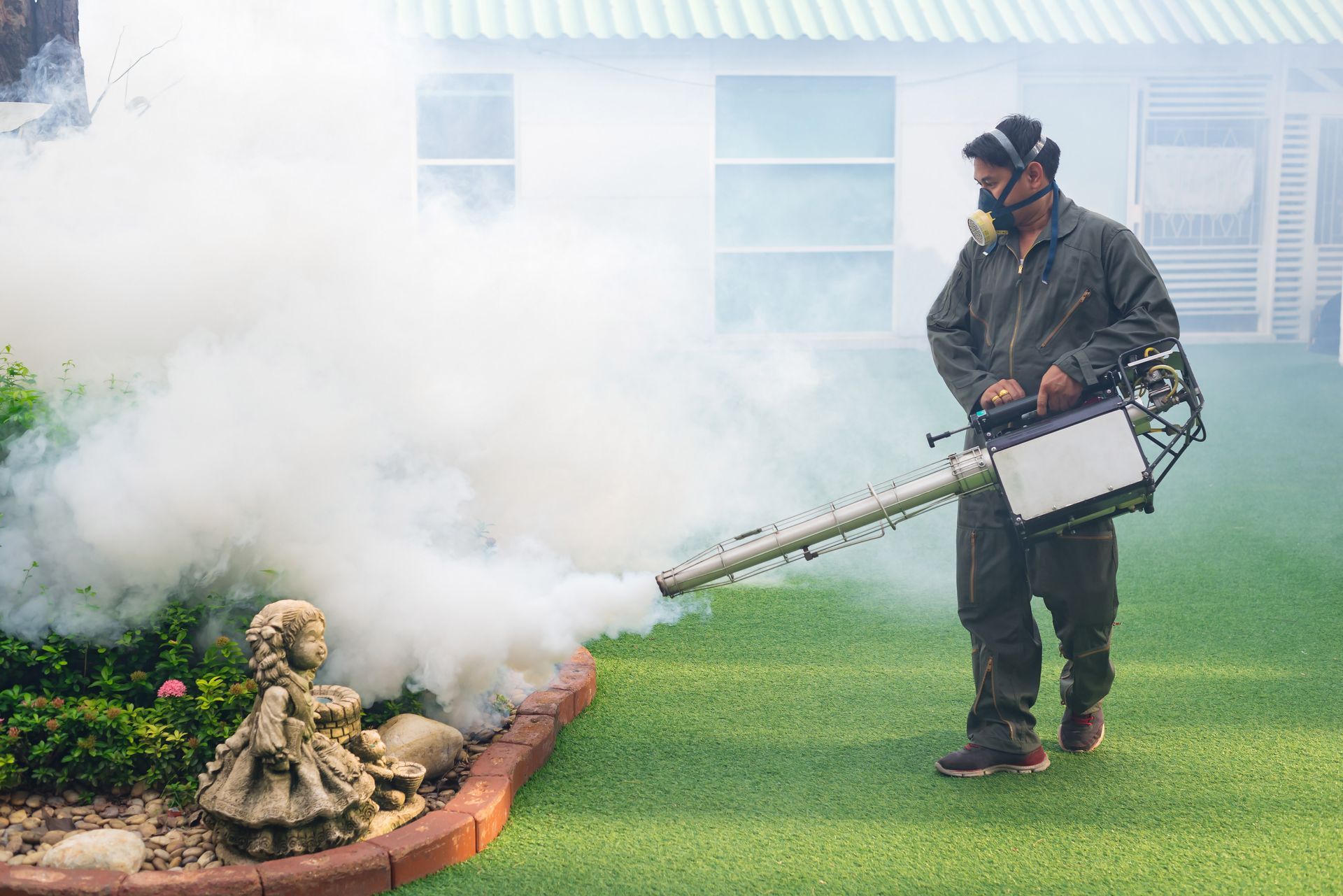 Man in protective suit spraying insecticide in a yard; smoke visible.