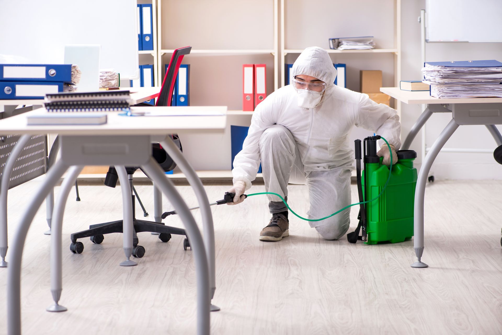 Person in protective suit spraying insecticide in an office.