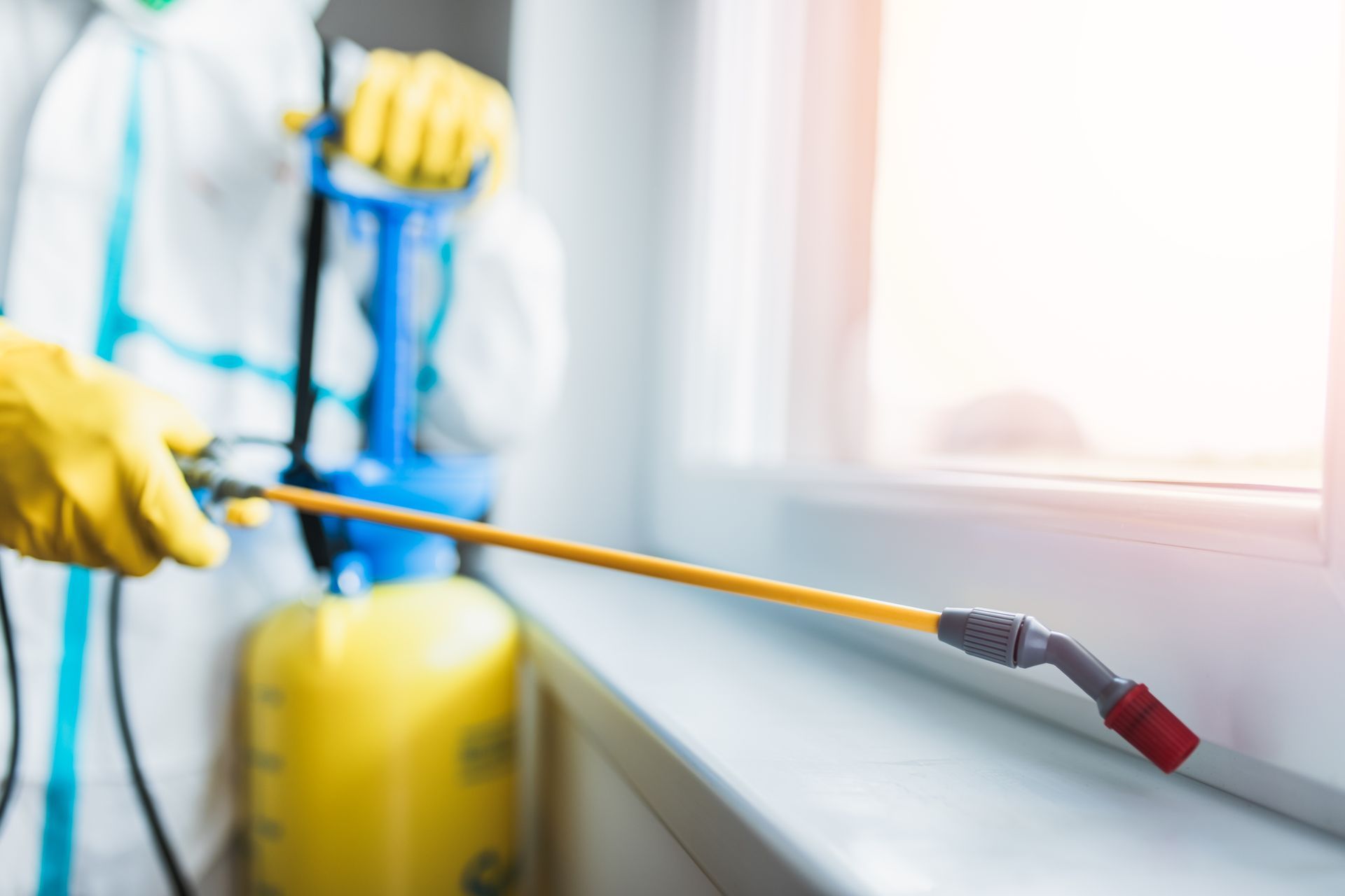Person in protective suit spraying insecticide near a window.