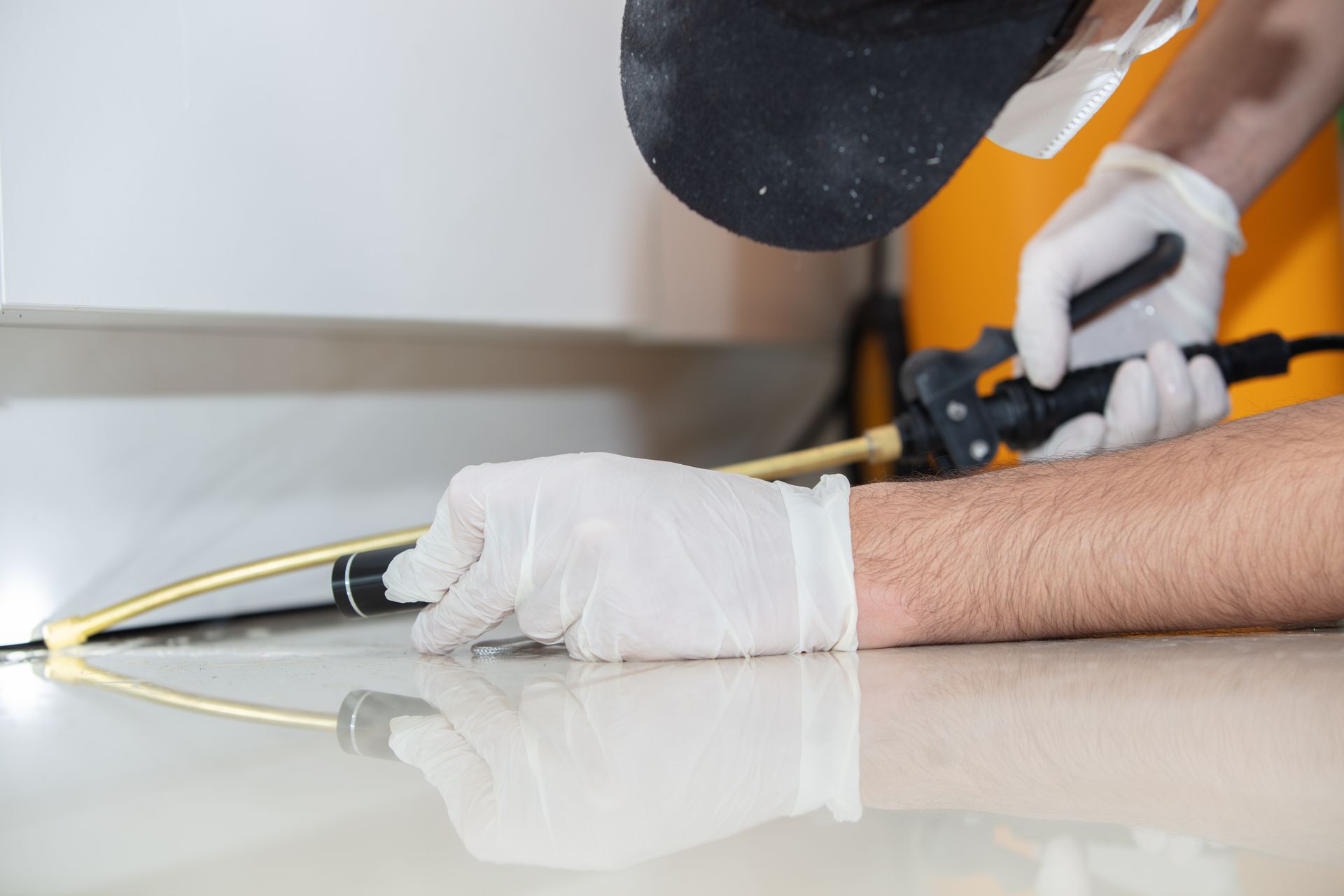 Person in gloves spraying insecticide on a white floor.