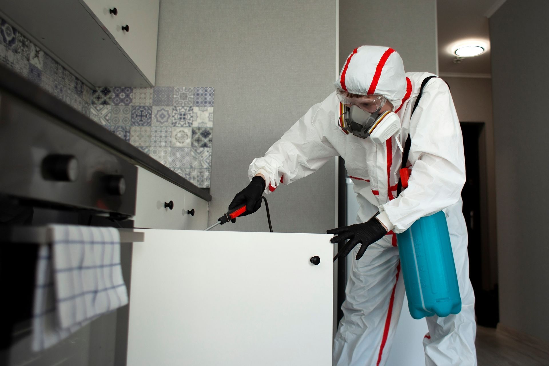 Person in protective suit spraying insecticide in a kitchen.