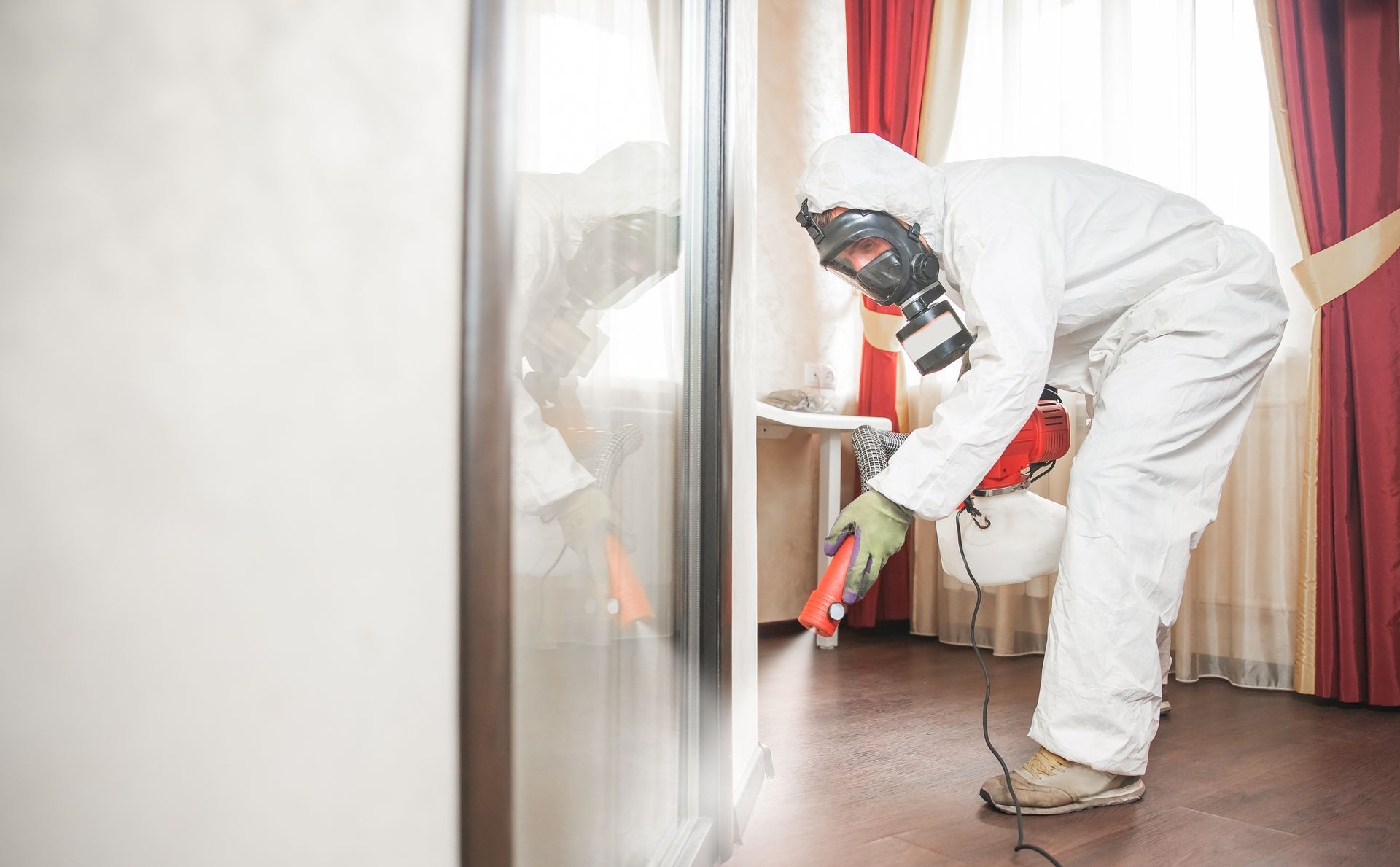 Person in hazmat suit spraying insecticide indoors.