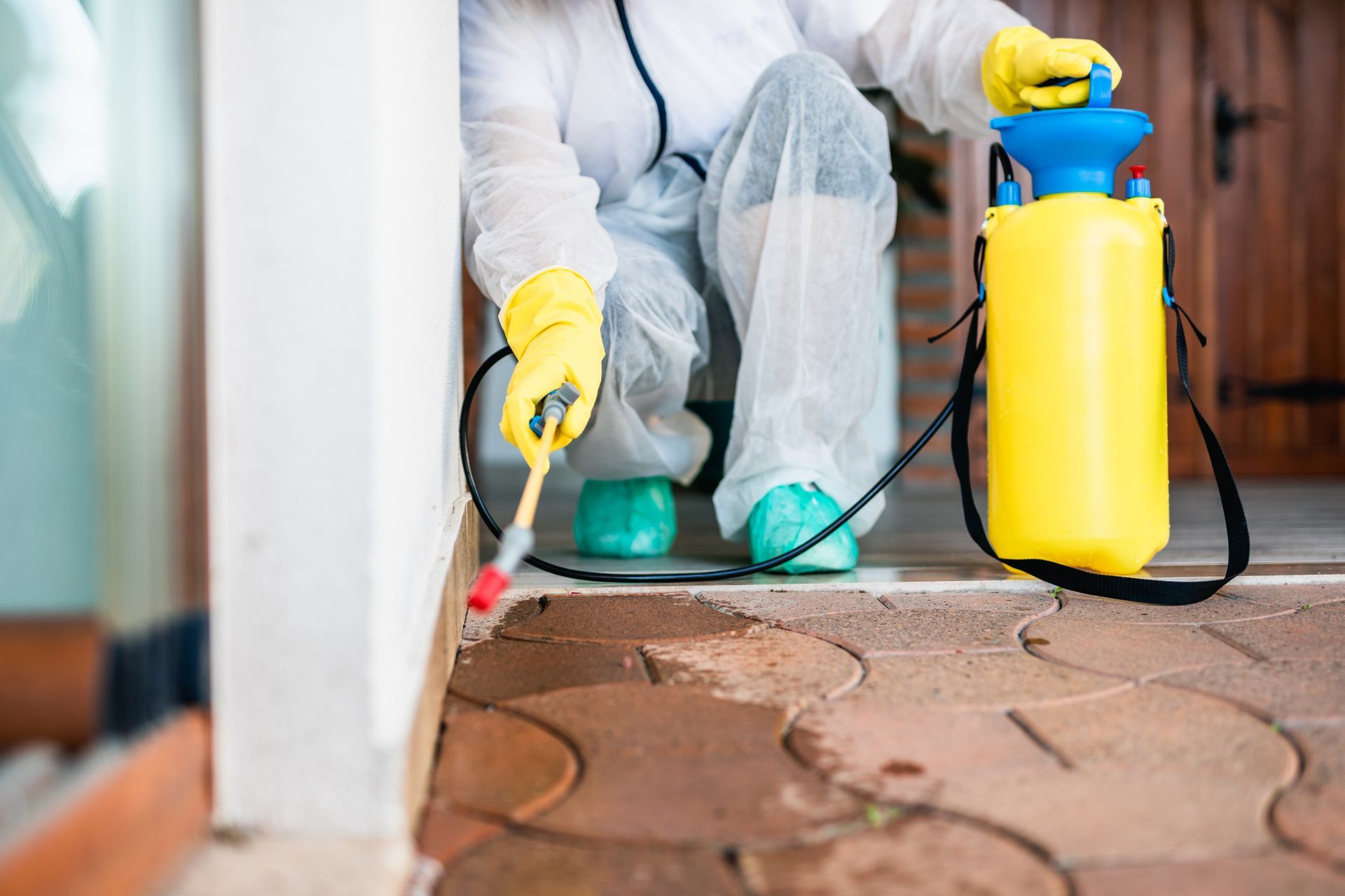 Person in protective suit spraying insecticide on a building's exterior.