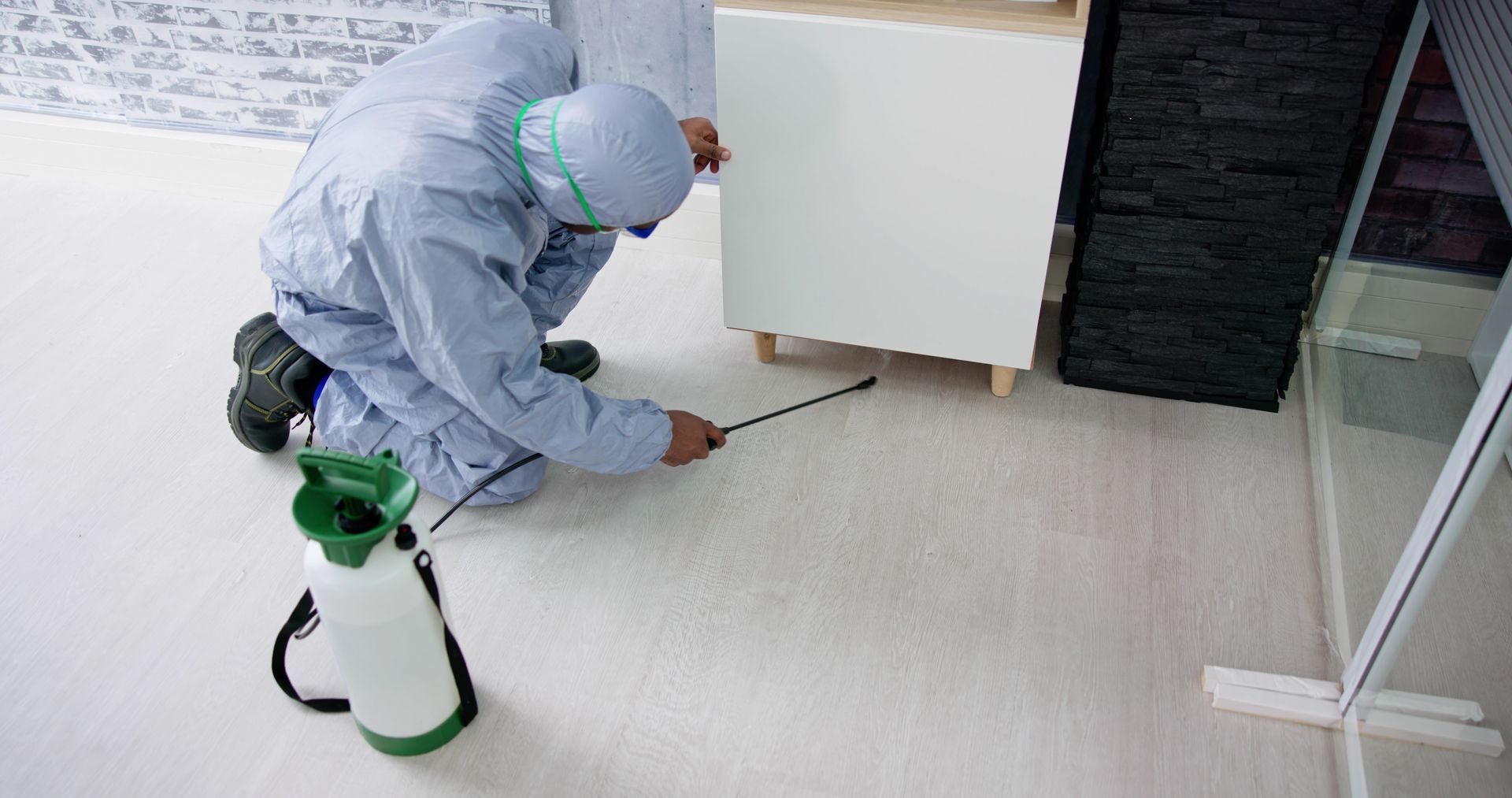 Person in protective suit spraying a pesticide on a floor.