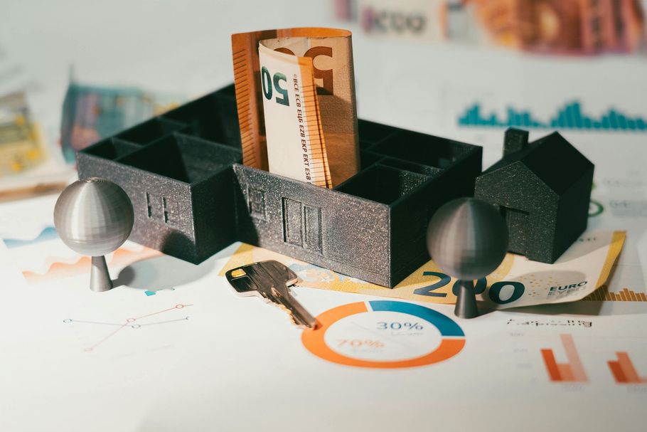 Paper currency tucked inside a 3D house model on a desk.