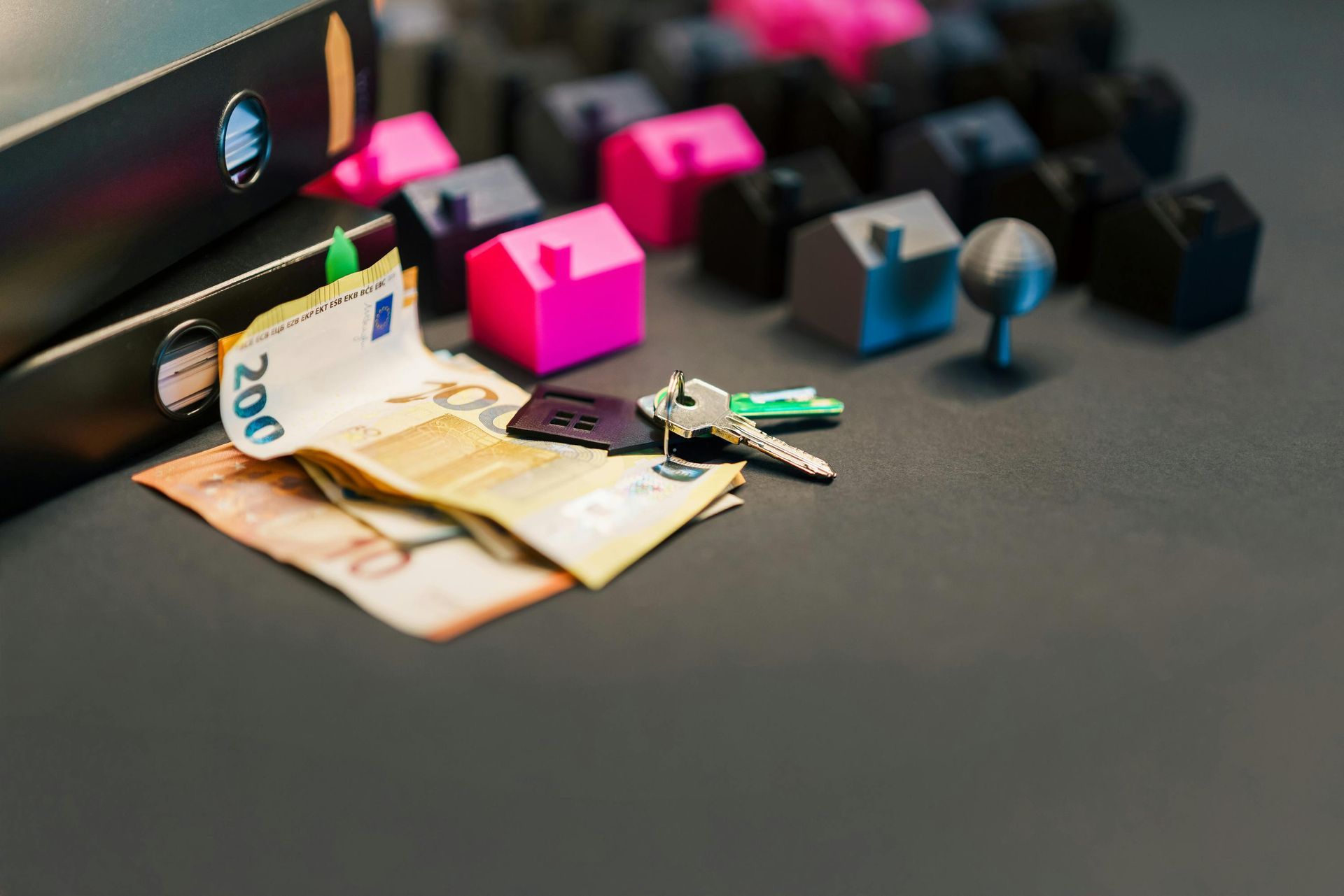 Euro bills and house keys surrounded by small colorful houses.