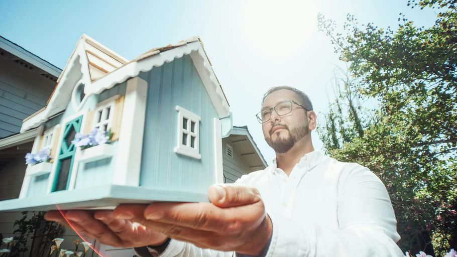 Man holding a small blue model house up toward the sky.