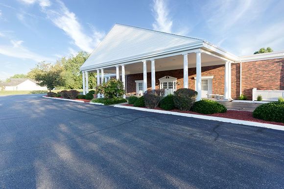 a large white building with a porch and a driveway in front of it .