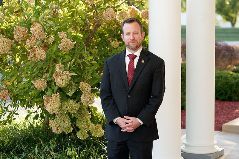 a man in a suit and tie is standing next to a white pillar .