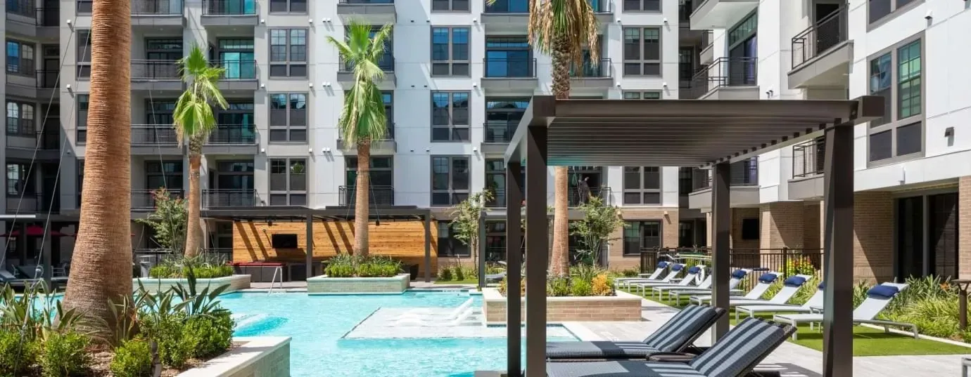 Resort-style swimming pool with lounge chairs and palm trees in a modern apartment complex.