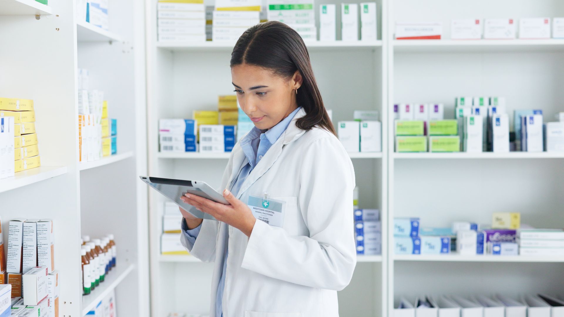 A female pharmacist is looking at a tablet in a pharmacy.