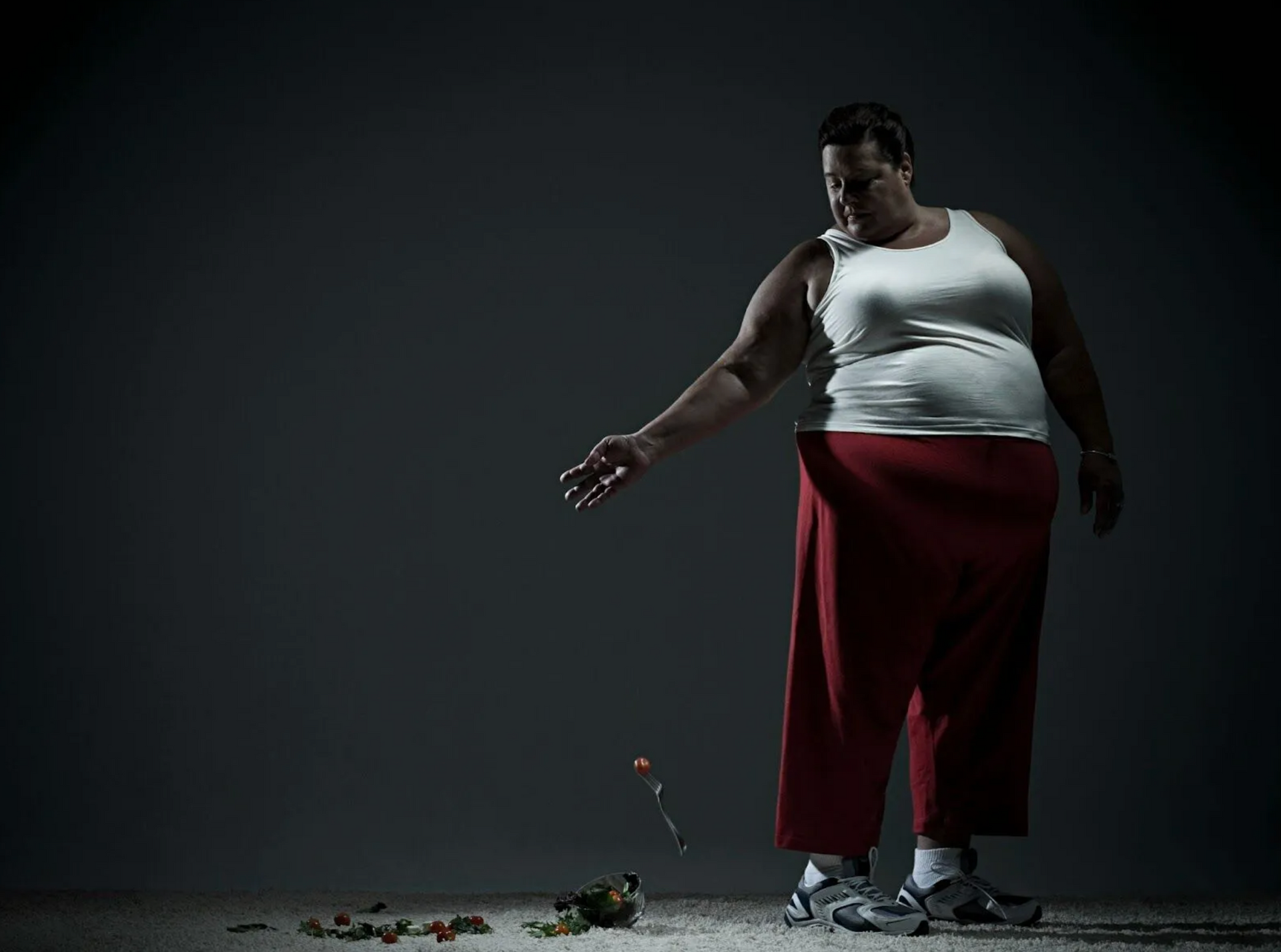 A woman in a white tank top and red pants is standing on the ground holding a flower.