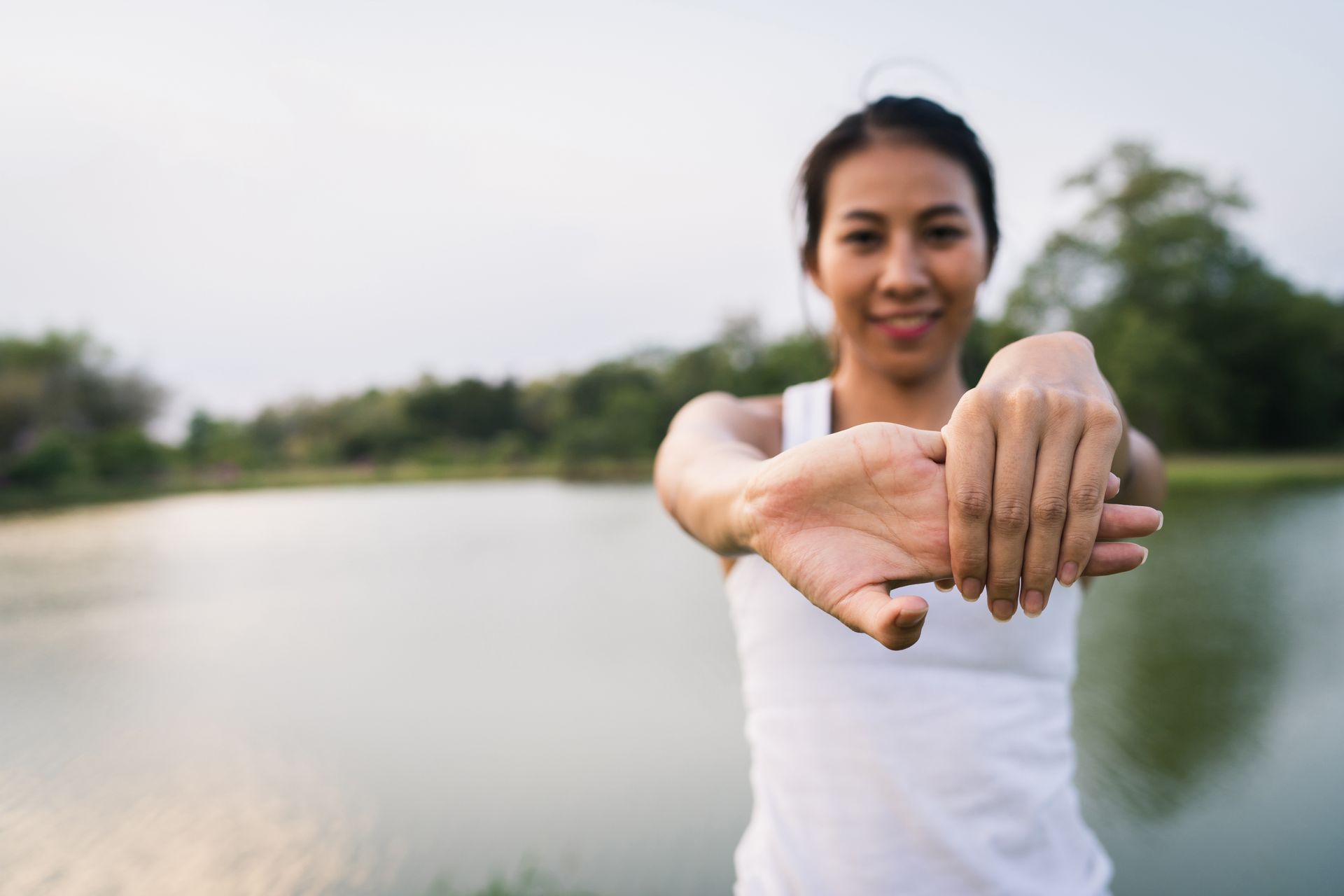 A woman is stretching her arms in front of a lake.