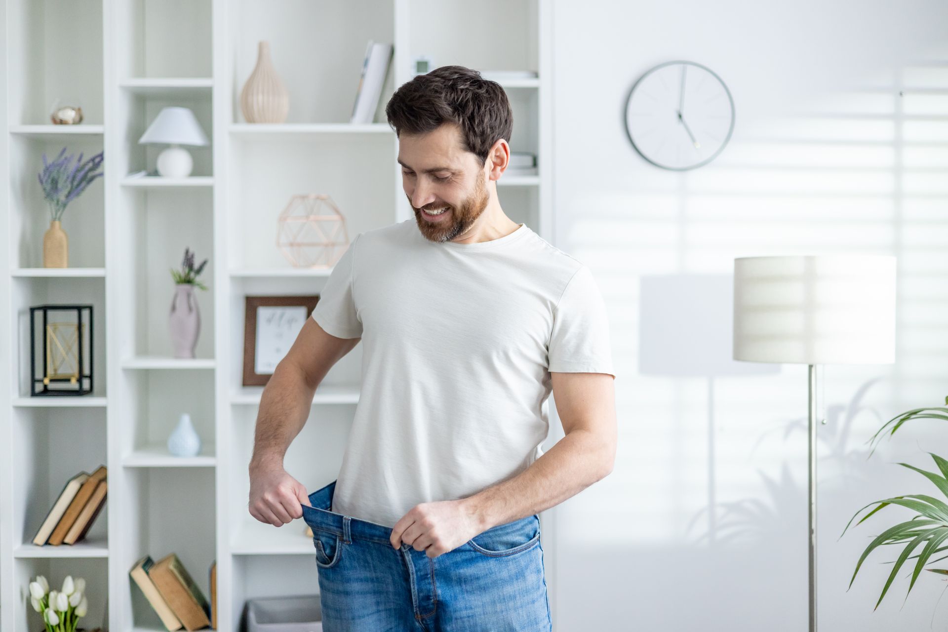 A man is standing in a living room looking at his pants.