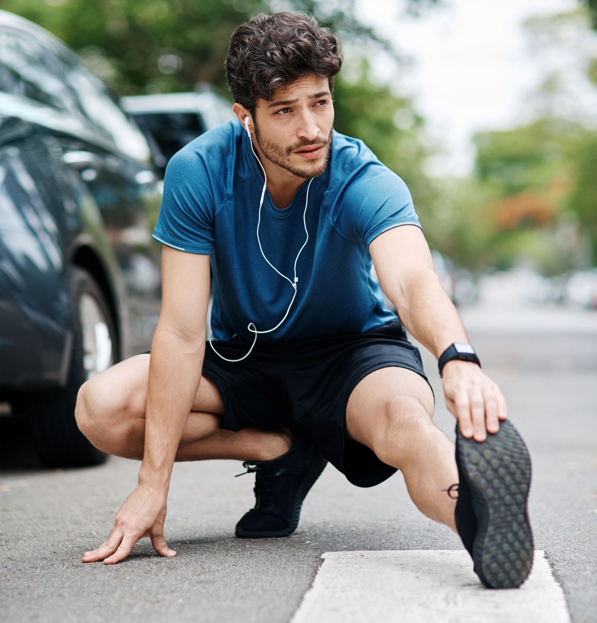 A man is sitting on the sidewalk stretching his legs.