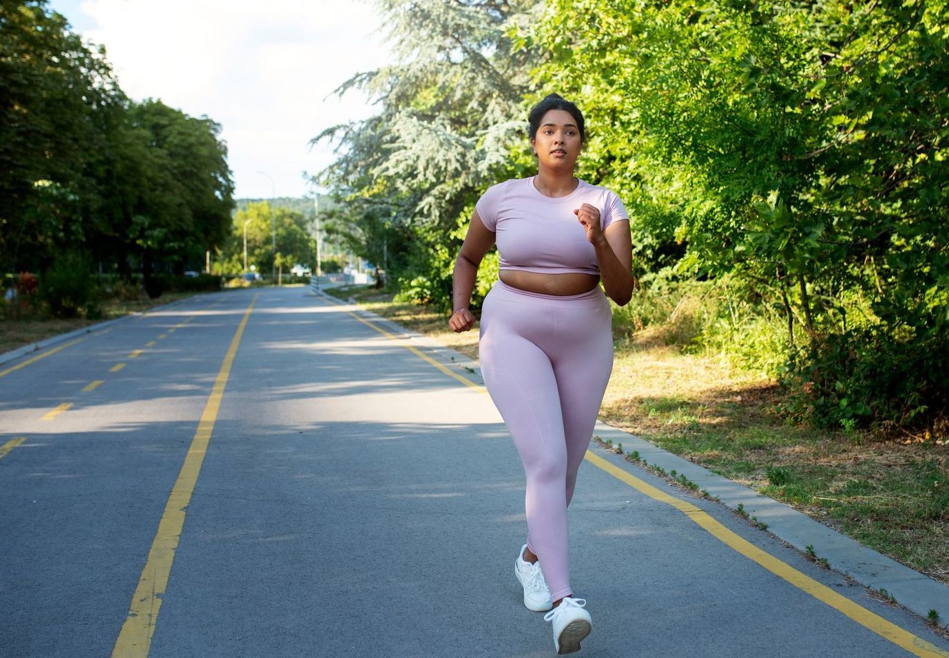 A woman is running down a road in a park.