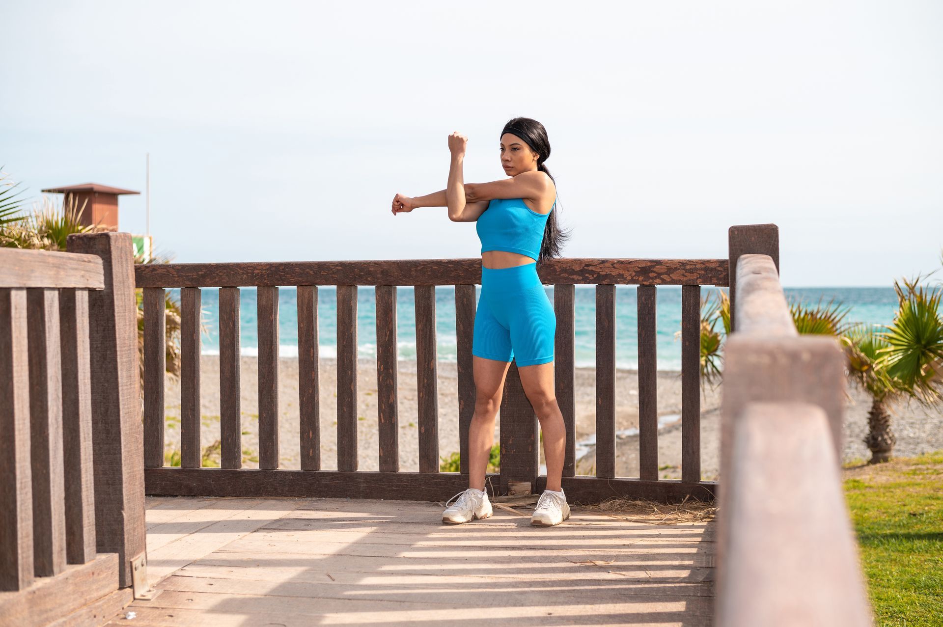 A woman is stretching her arms on a pier near the ocean.