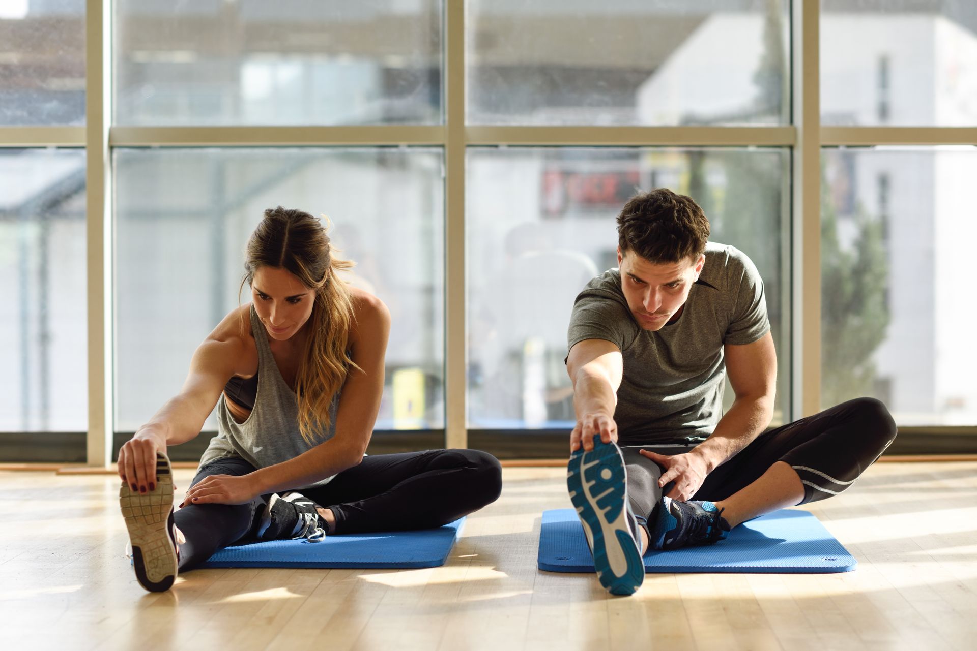 A man and a woman are stretching on yoga mats in a gym.