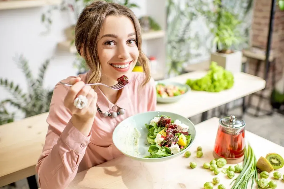 A woman is sitting at a table eating a salad with a fork.