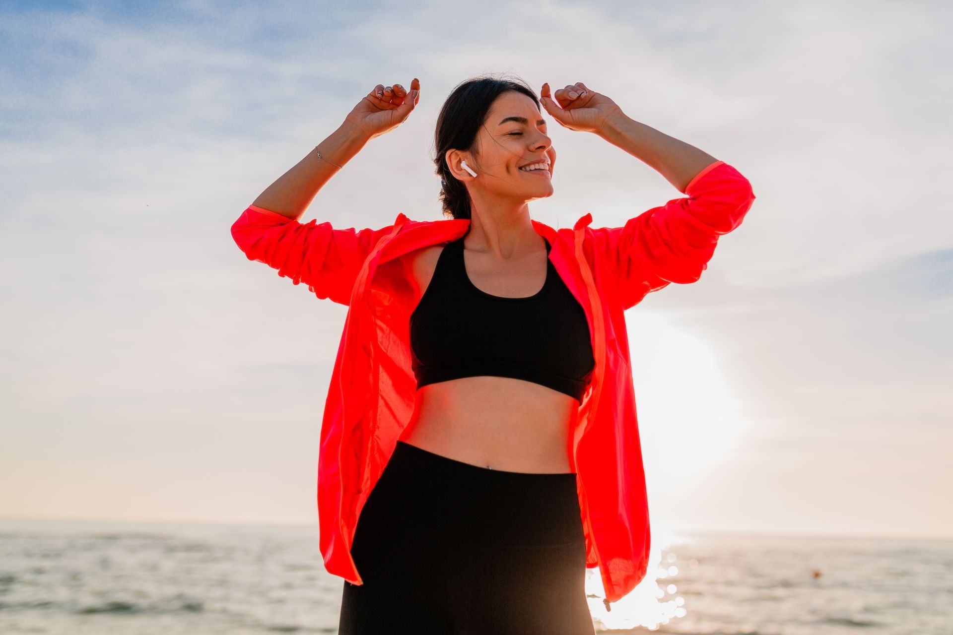 A woman is standing on the beach with her arms in the air.