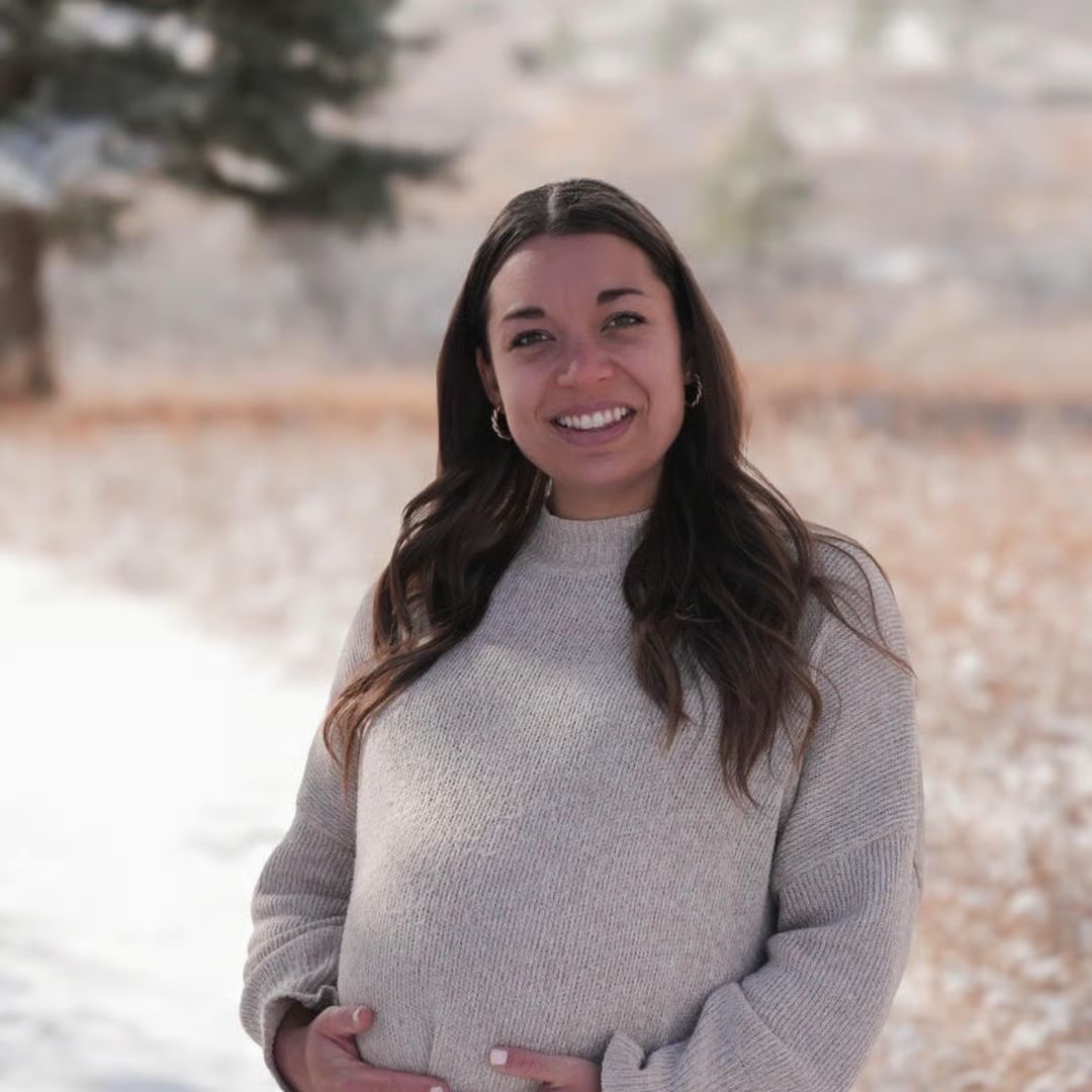 Woman smiling in a snowy outdoor setting, wearing a light gray sweater.