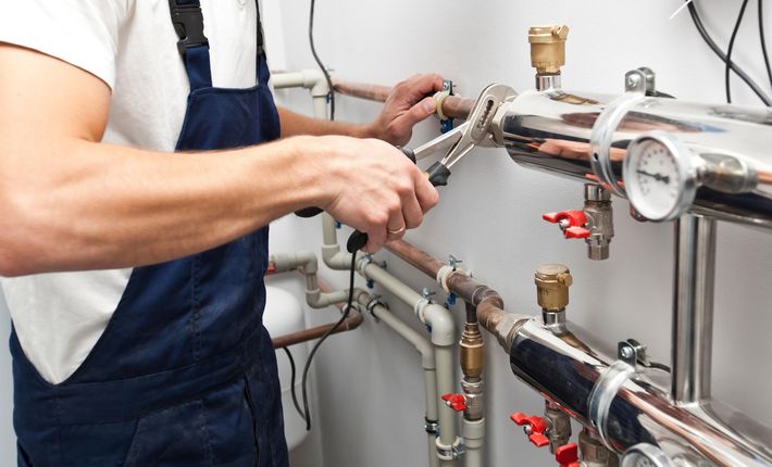 A technician in navy overalls uses a wrench to tighten a pipe fitting on a commercial plumbing system.