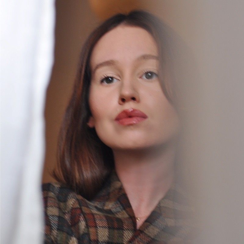 Woman with auburn hair pouting at the camera, wearing a plaid shirt.