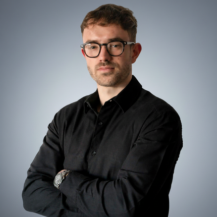 Man with glasses, arms crossed, wearing a black button-down shirt, neutral expression.