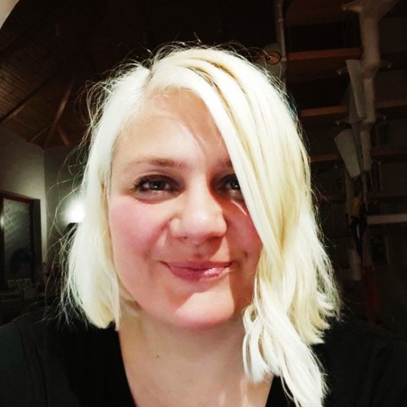 Woman with white hair smiling indoors, wearing a black shirt.