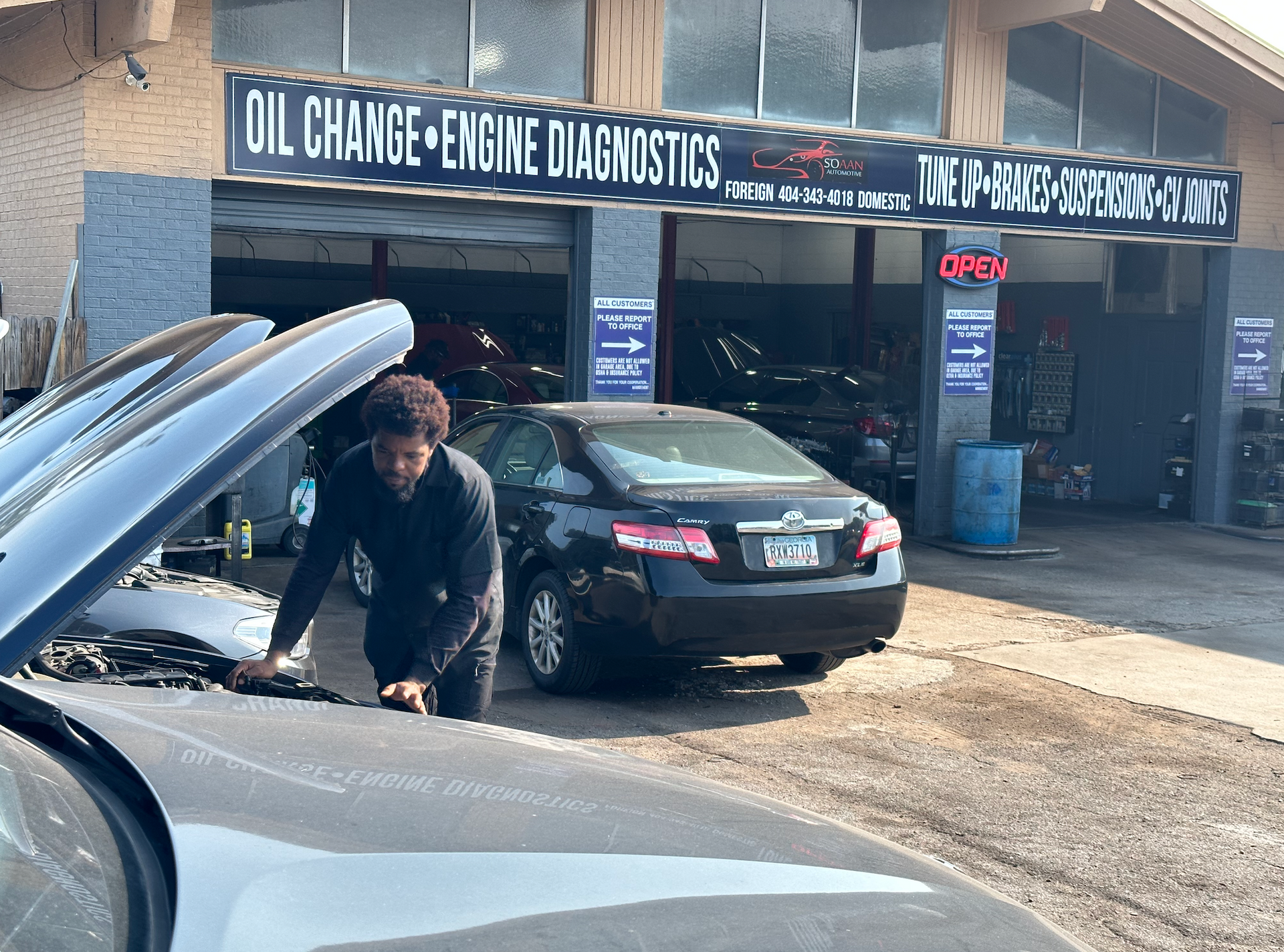 A man looking under the hood of a car in front of a building that says oil charge engine diagnostics