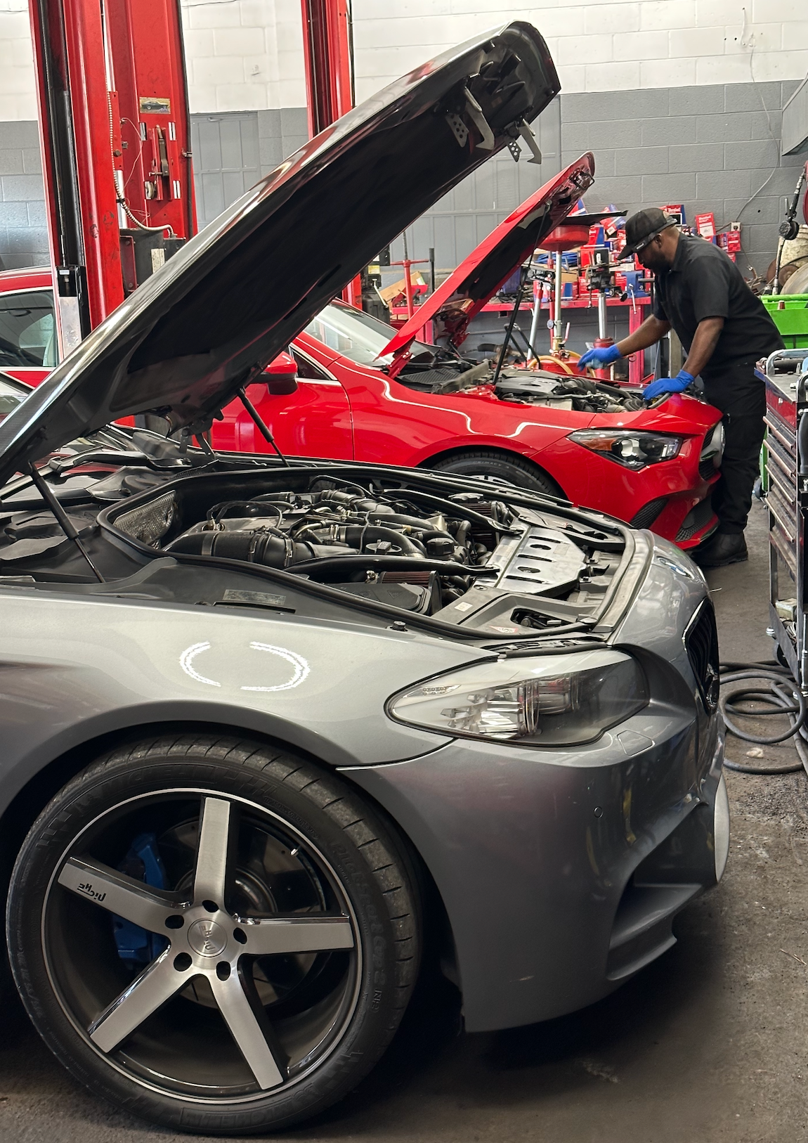 A man is working on a car in a garage with the hood open.