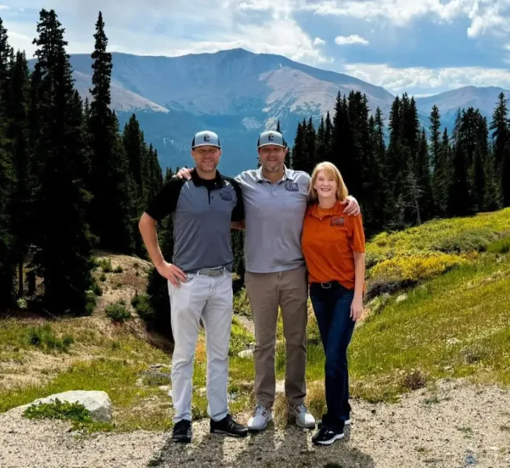 Three people posing for a picture with mountains in the background