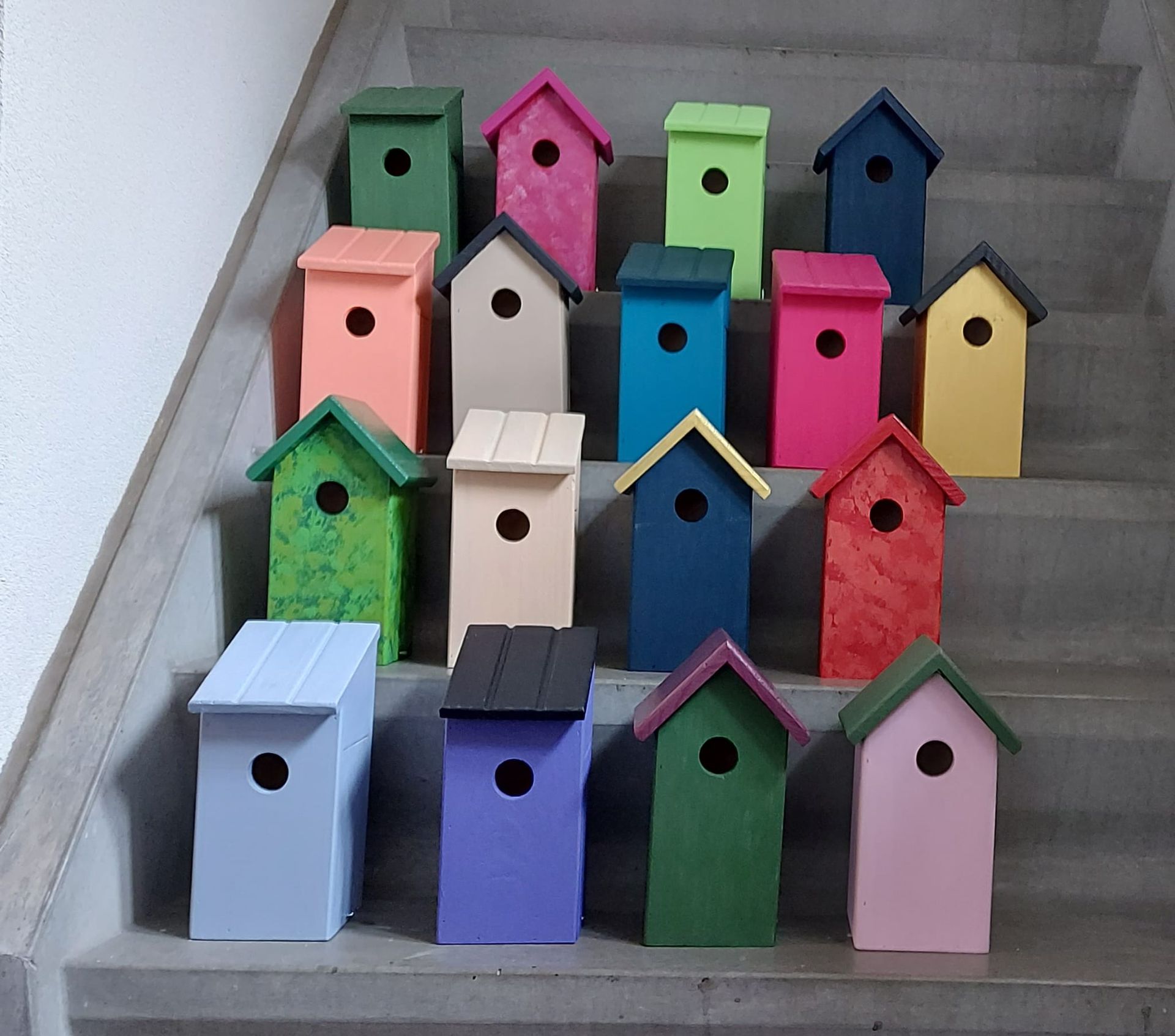 Op betonnen trappen staan ​​kleurrijke vogelhuisjes in verschillende vormen en maten opgesteld.