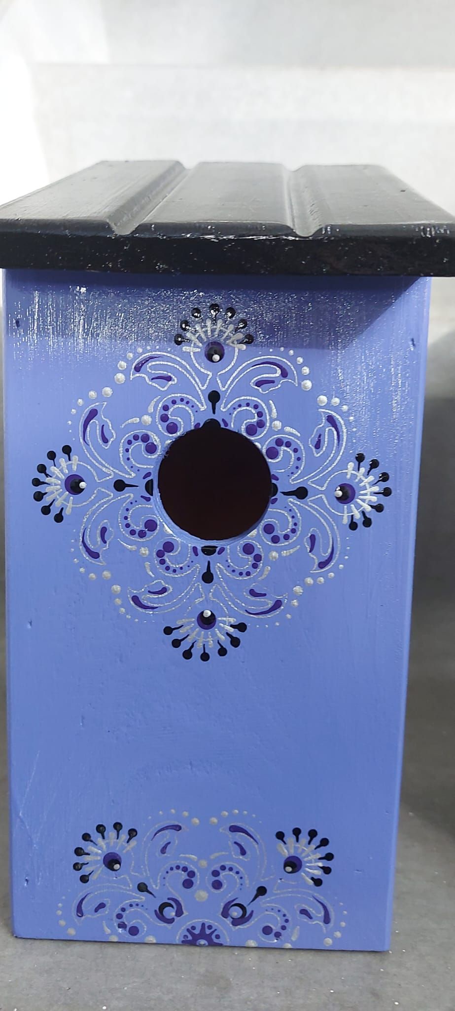 Blauw vogelhuisje met een donker dak en decoratieve uitsparingen.