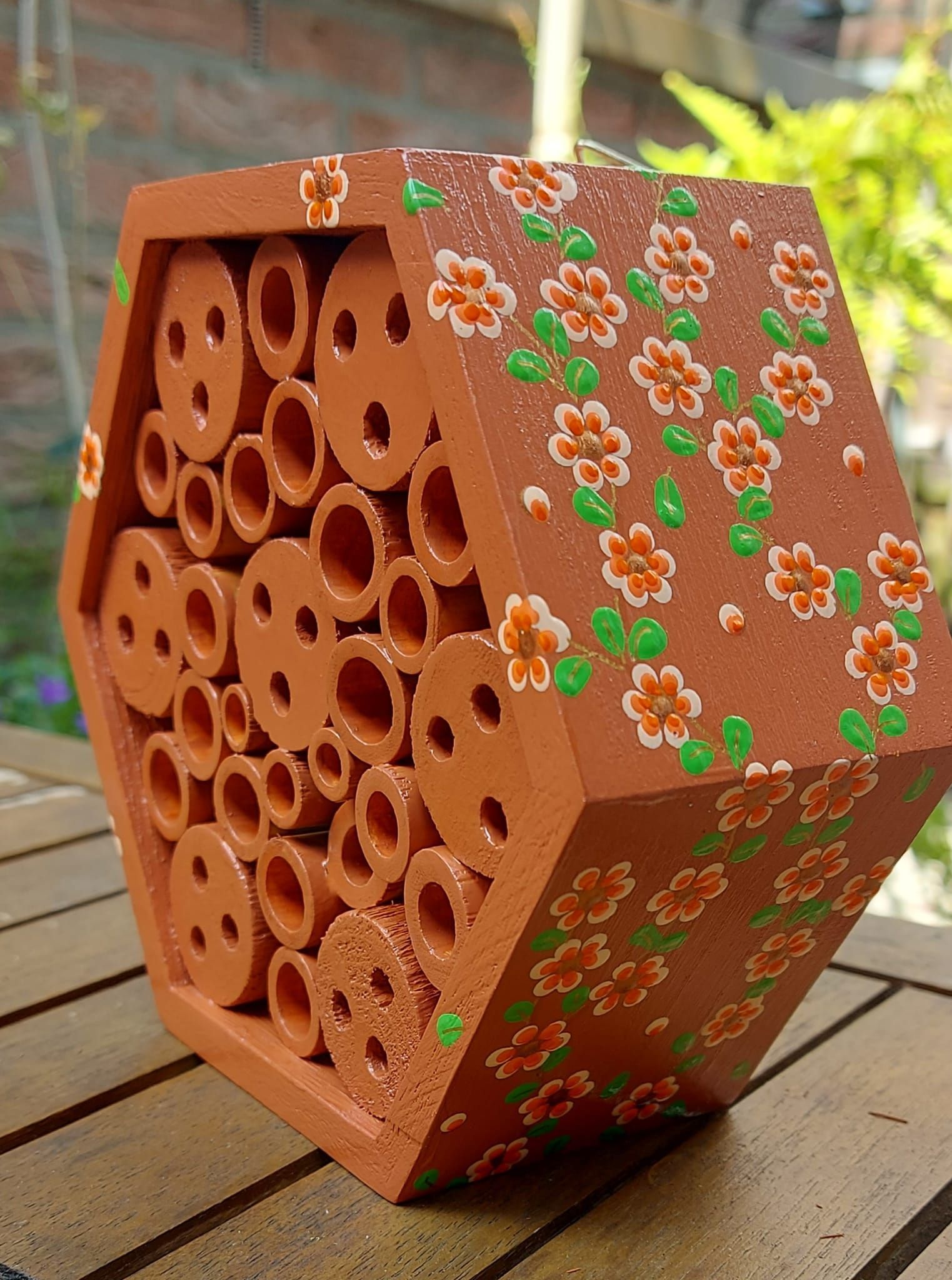 Zeshoekig, terracottakleurig bijenhuis met openingen, versierd met oranje bloemen en groene bladeren.