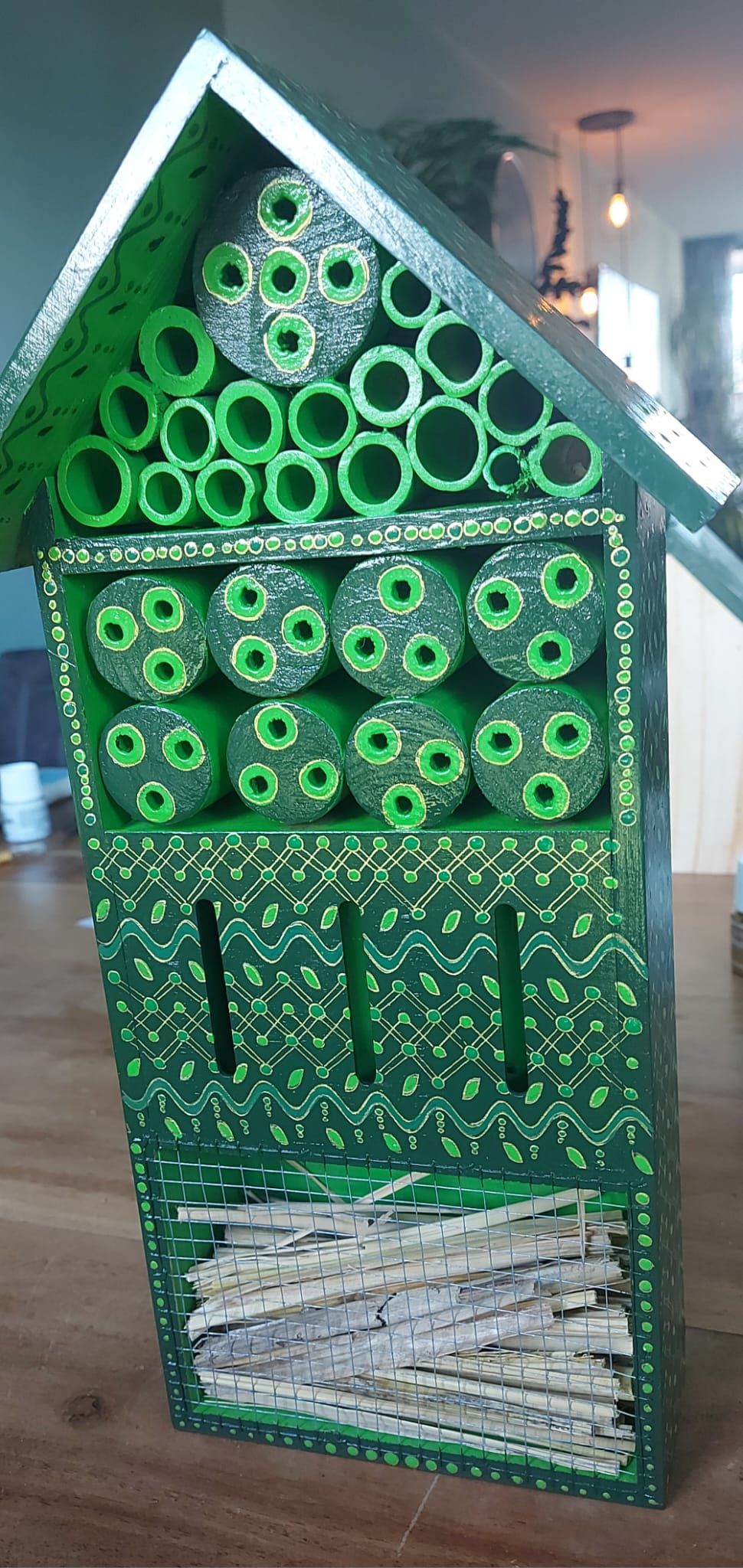 Groen houten insectenhotel met diverse nestcompartimenten.