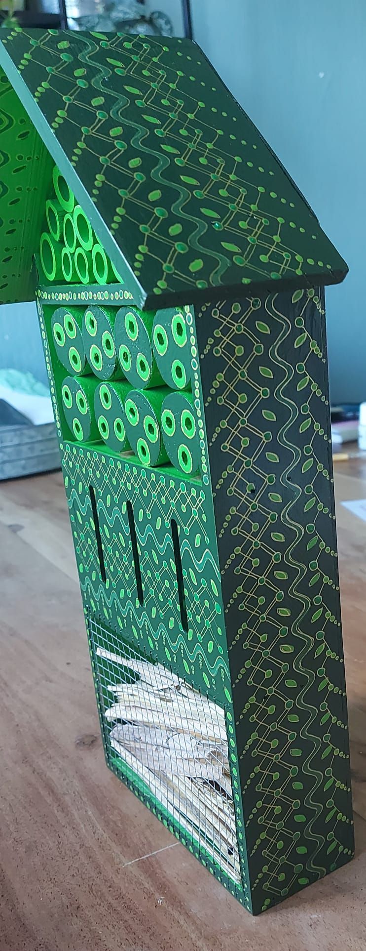 Groen vogelhuisje met patroon en dak, geplaatst op een houten ondergrond.