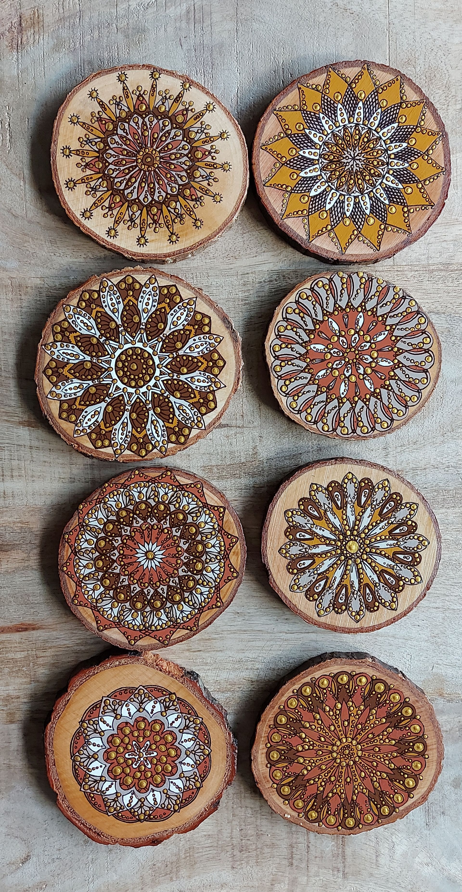 Acht ronde houten onderzetters met ingewikkelde, kleurrijke mandala-ontwerpen.