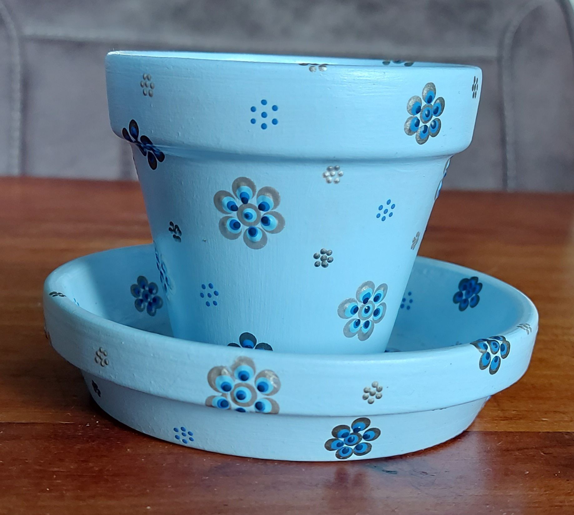 Lichtblauwe bloempot met schotel, versierd met blauwe en zilveren bloemmotieven.