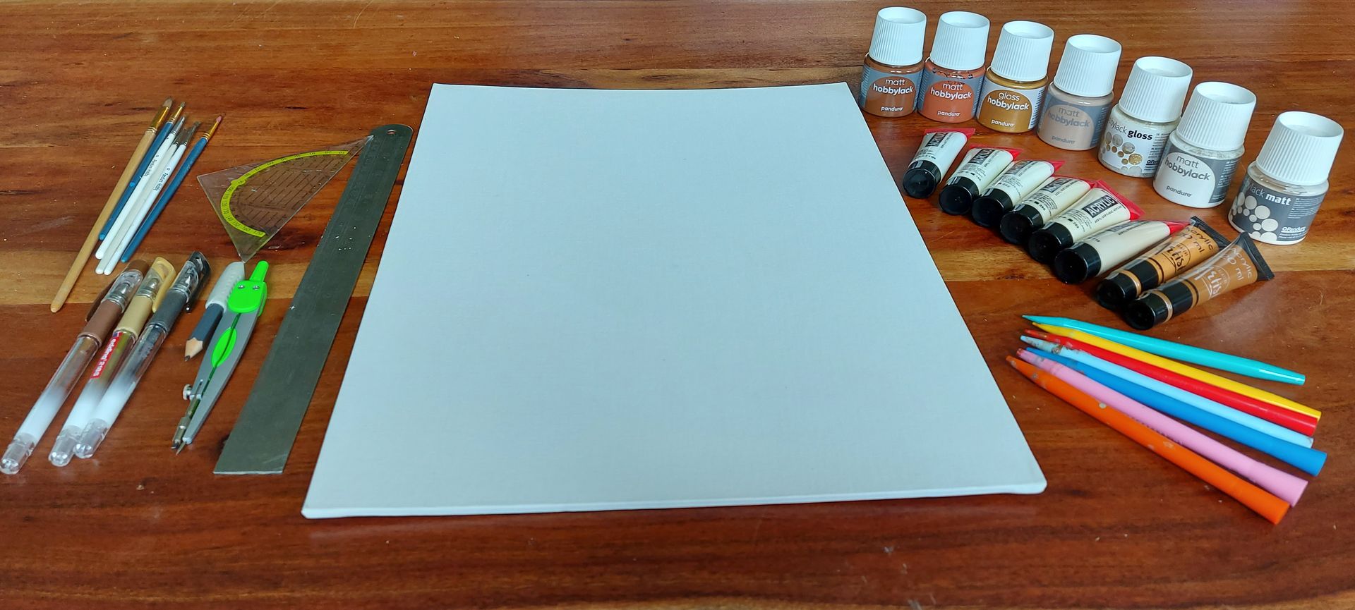 Teken- en schildermaterialen uitgestald op een houten ondergrond: papier, potloden, verf, linialen en diverse gereedschappen.