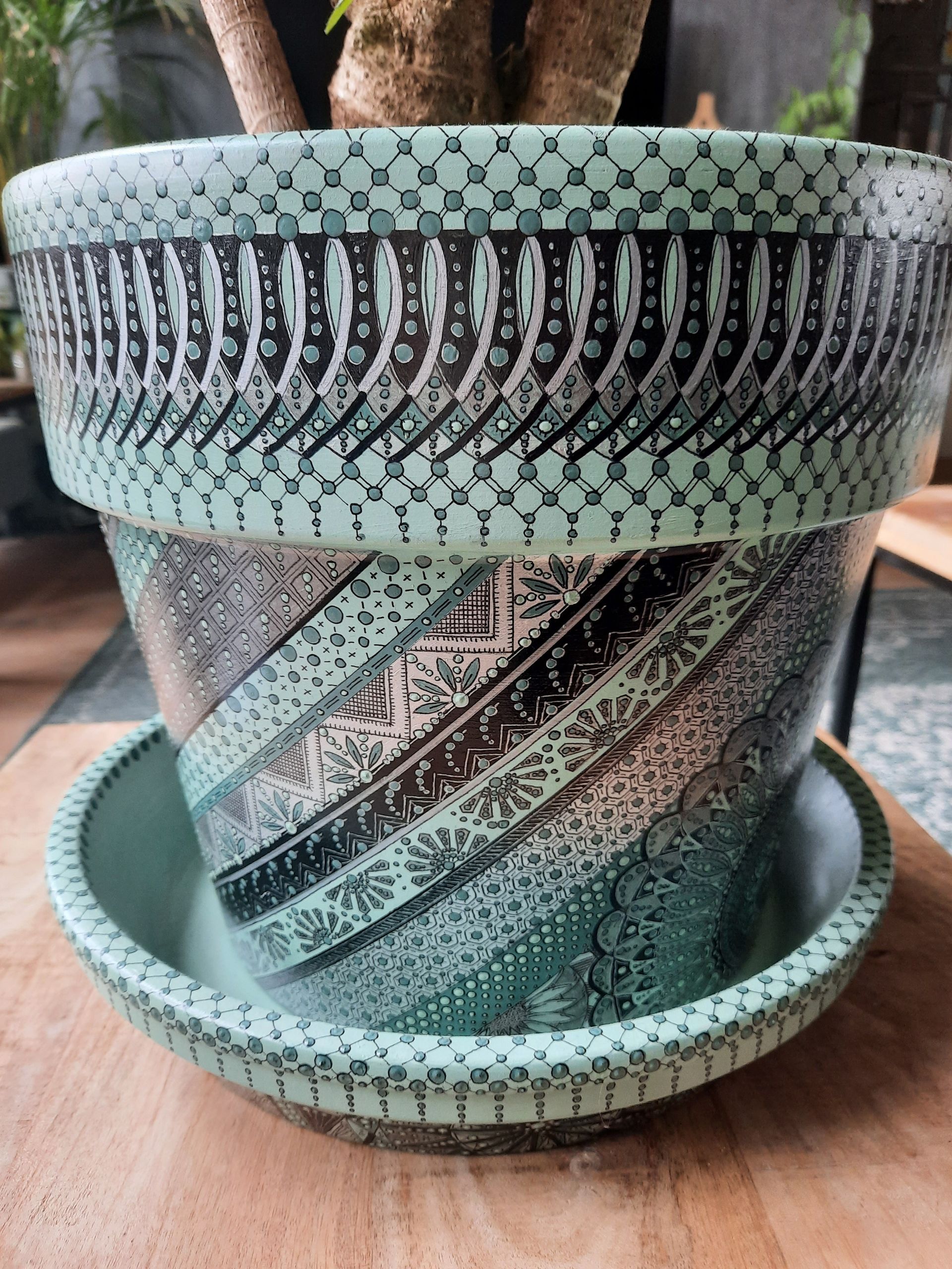 Aqua en zwart patroon keramische bloempot met schotel op een houten ondergrond.