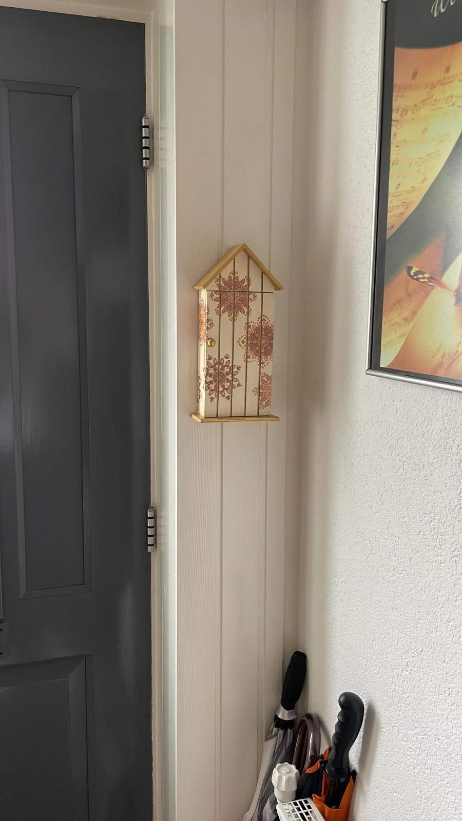 Een decoratieve houten sleutelhouder met bloemmotieven op een witte lambrisering