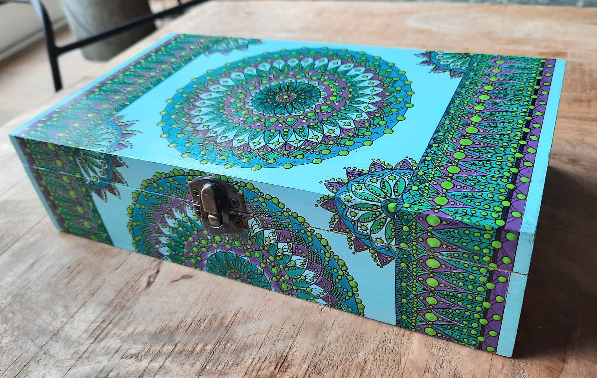 Aquakleurige doos met mandala-patroon en sluiting, op een houten ondergrond.